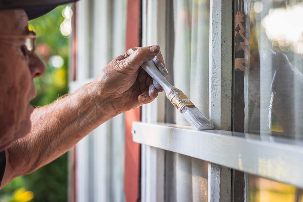 En äldre man målar ett vitt fönster
